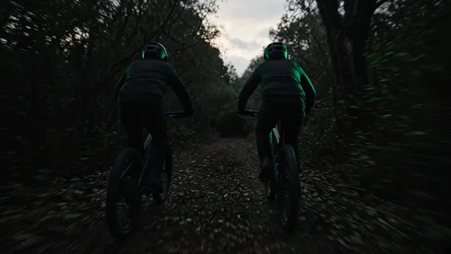 Two riders racing electric mountain bikes down a forest trail at dusk